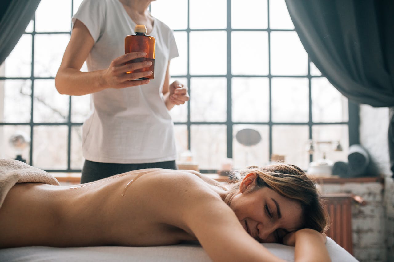 A woman enjoying a relaxing massage in a serene spa environment, holding a bottle of essential oil.